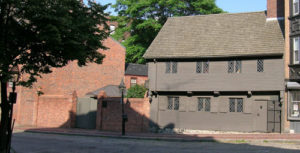 Modern photograph of a brown wooden house with diamond pane windows and a steep roof