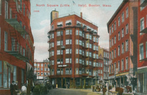 Postcard of a city block. Large brick buildings with shoppers and bystanders walking the streets.