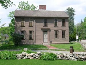 A brown, wooden house with 9 windows and a light colored front door.