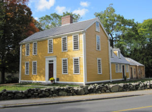 Two story, yellow, wooden sided home with trees in the background