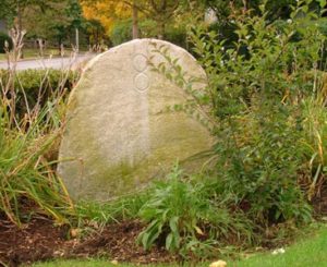 Curved stone with the number 8 etched into it surrounded by brush