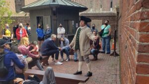 man dressed in colonial clothing speaking to a crowd of people