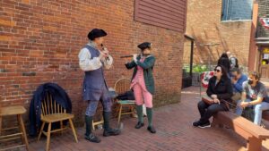 two people wearing colonial clothing and playing wind instruments