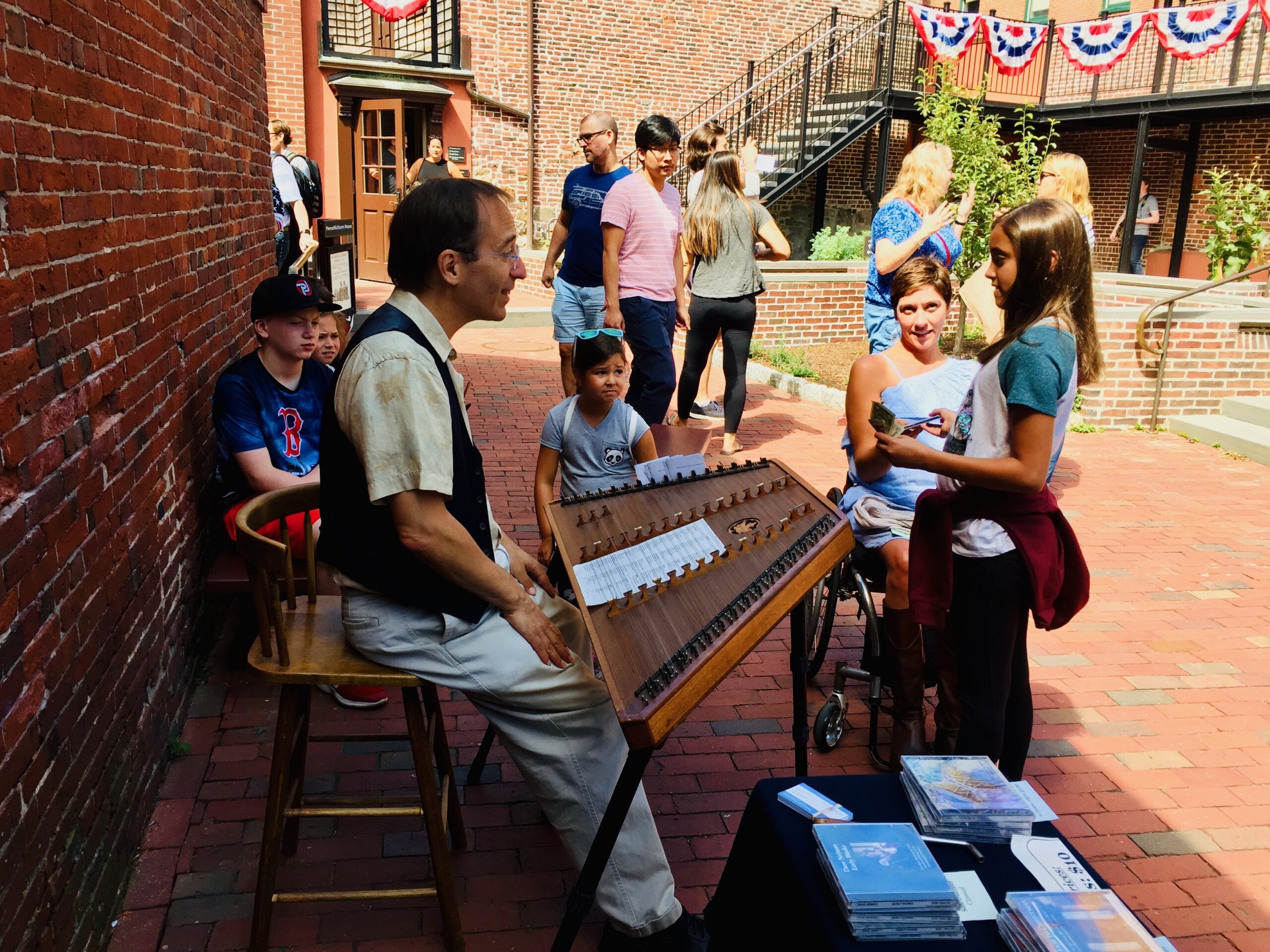 A white middle-aged man playing the hammered dulcimer in the Revere House courtyard for a crowd of visitors