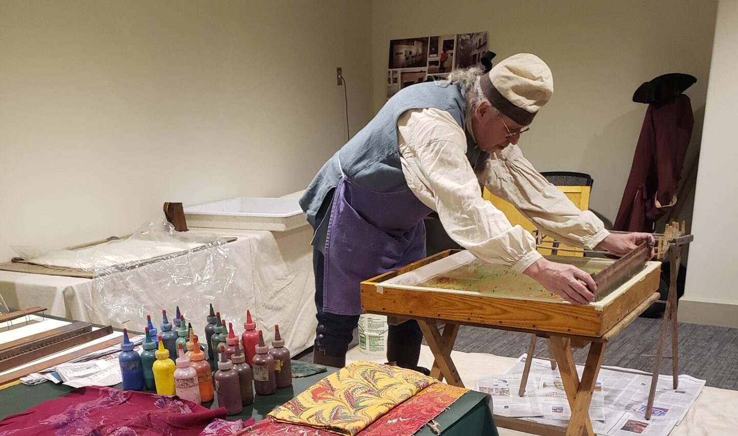 a man in colonial dress hand-coloring paper