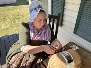 a woman in colonial clothing making lace by a traditional method